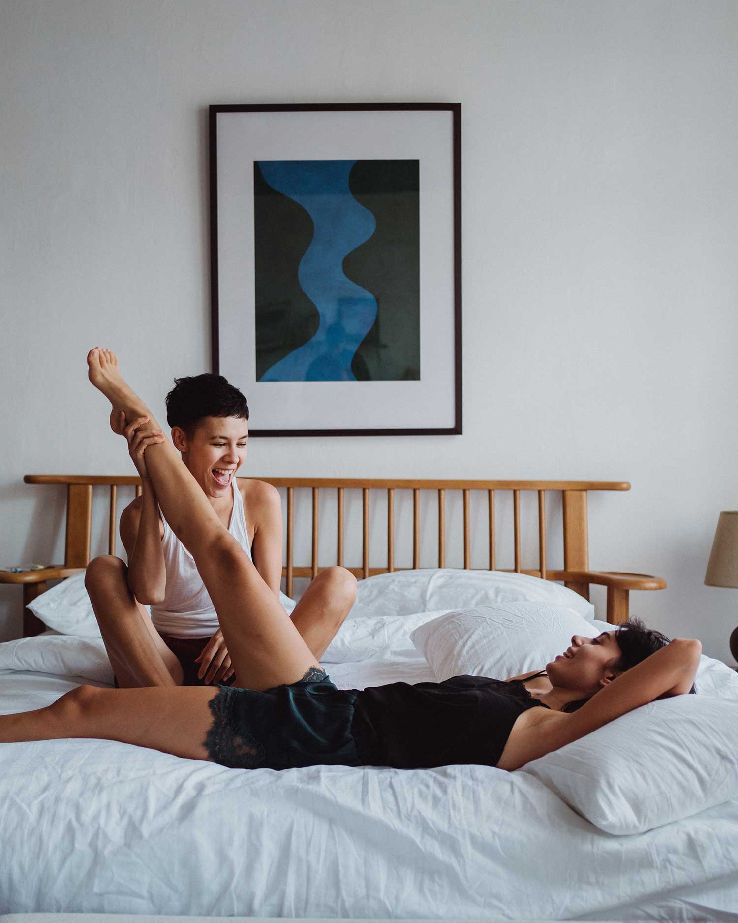 Two people laughing and playing together on a bed in a bright, airy room
