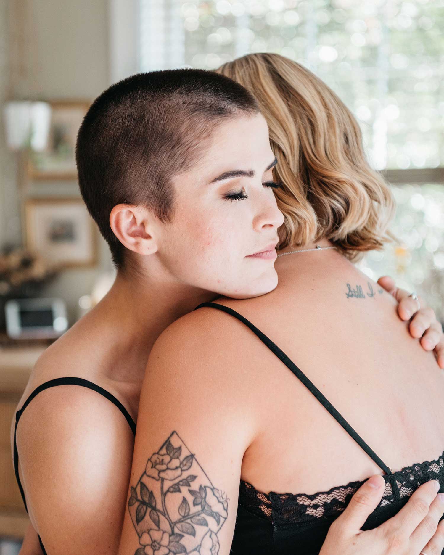 Two people in a tender, close embrace with eyes closed, both with visible tattoos