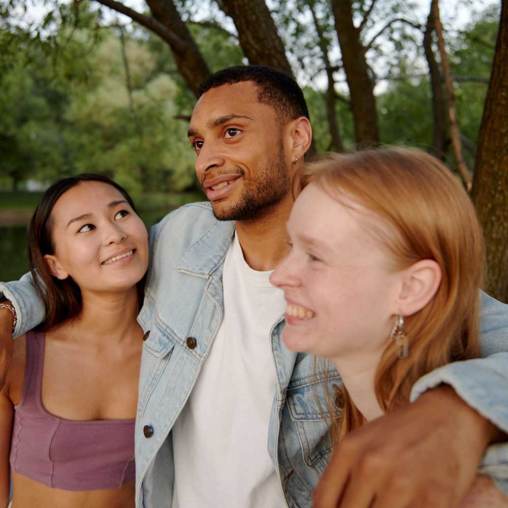 Three people smiling and laughing together outdoors with their arms around each other
