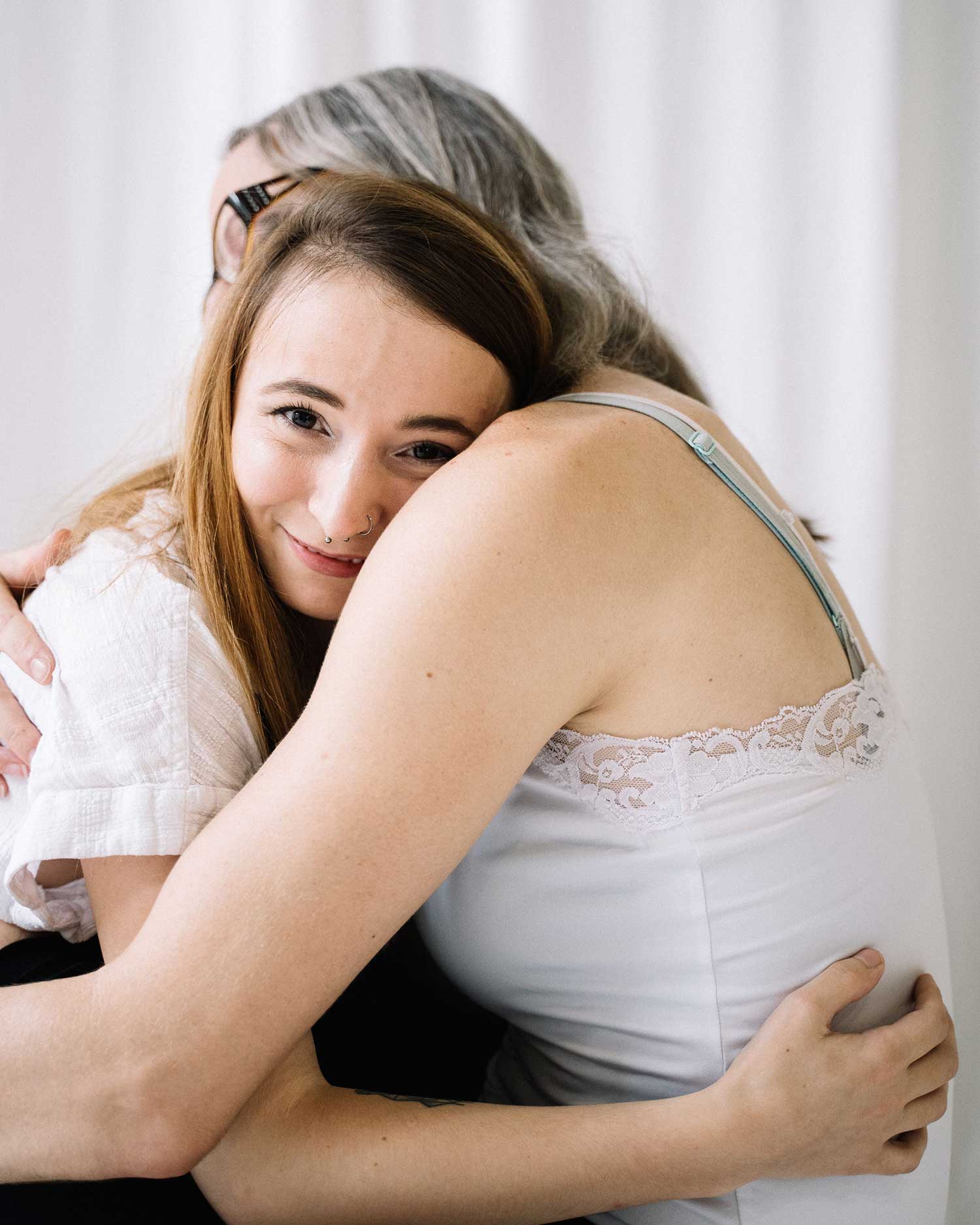 Two women sharing a warm, close hug, one smiling softly with a look of contentment