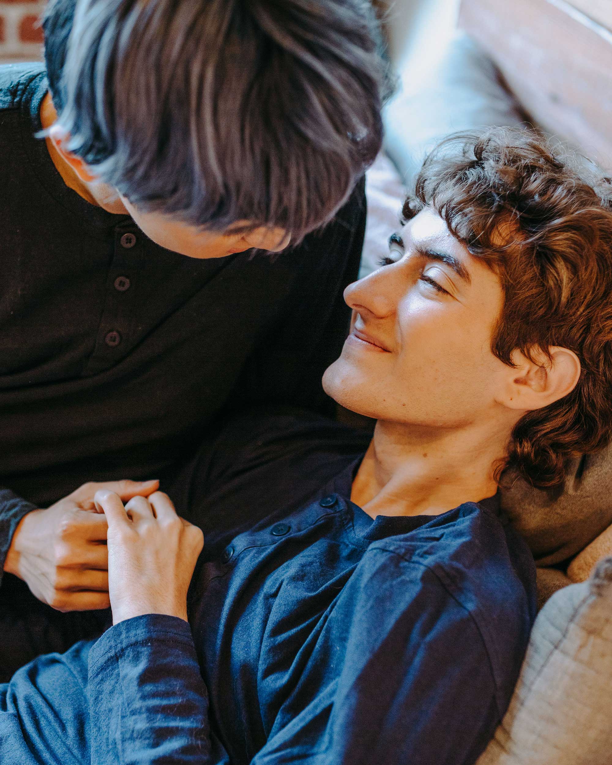 Two people sharing an affectionate moment together, one resting back while the other leans close, holding hands